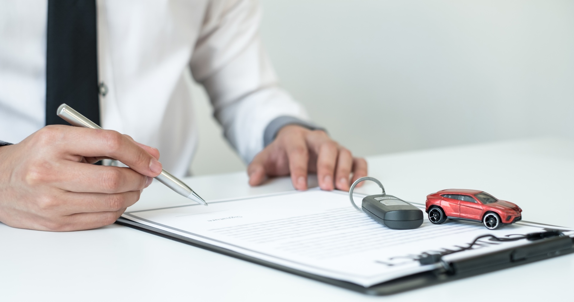 Persona firmando un contrato sobre el que hay un coche en miniatura y una llave de coche